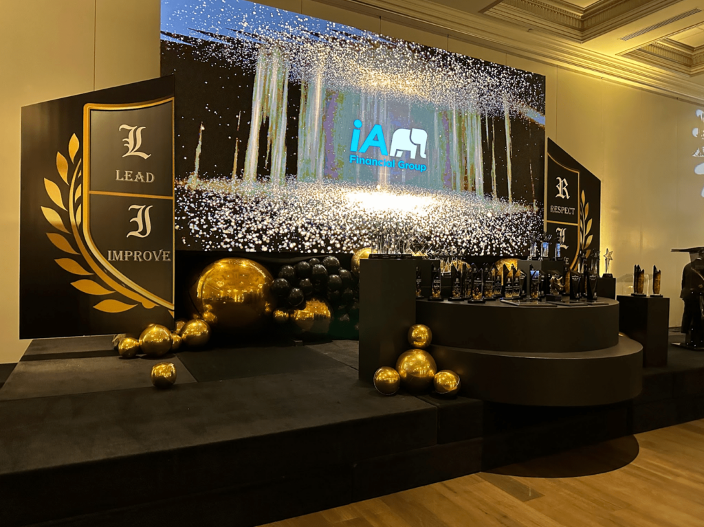 iA Financial Group award ceremony stage with a large LED screen displaying glittering visuals and branding, surrounded by gold and black decor and trophies.